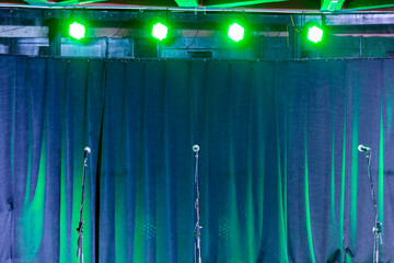 Microphones on stands on the stage against a background of curtains.