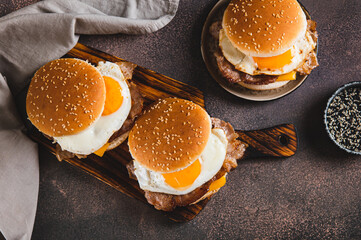 Burgers with fried egg, bacon and cheese on a board on a table top view