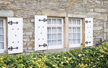 Wooden windows with white shutters on old stone cottage, UK