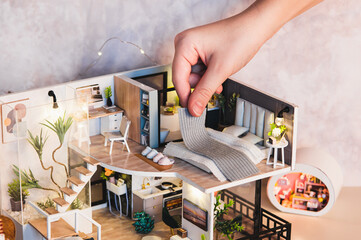 A child's hand puts a blanket on a bed on the second floor of a tiny house on a table
