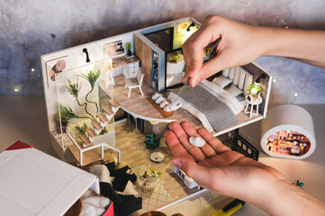 Children's hands place slippers next to the bed in a tiny roombox.