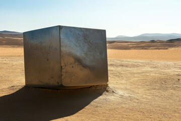 Shiny metal monolith casting a shadow on the dry desert ground under blue sky