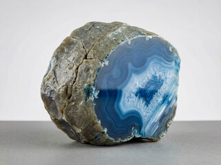 Natural blue agate geode specimen with concentric banding and a crystalline quartz core on a gray surface.