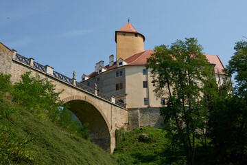 Fototapeta premium Brno, Czech Republic - August 16, 2025 - Veveri Royal Castle - Historic castle with arched bridge and lush green trees under a clear blue sky