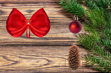 A fresh Christmas tree branch on a wooden background. A New Year's collage of Christmas decorations, a red bow, and a pine cone.