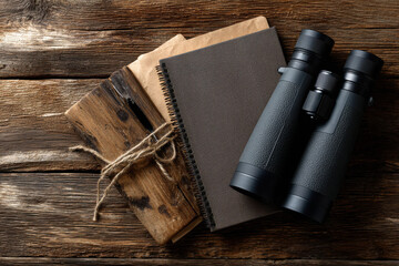 Outdoor adventure gear with binoculars and notebooks on wooden table