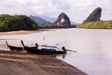 Long tail boats moored on a calm river in Krabi, Thailand with limestone karst mountains and tropical mangroves
