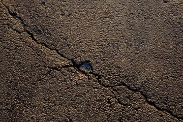 Cracked asphalt road surface in warm evening light, close up of damaged pavement with small pothole, concept of infrastructure wear, street maintenance and transport safety background.