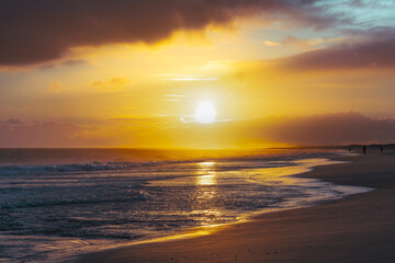 The glowing sun sets over the ocean, reflecting warm hues across the gentle waves and sandy beach.