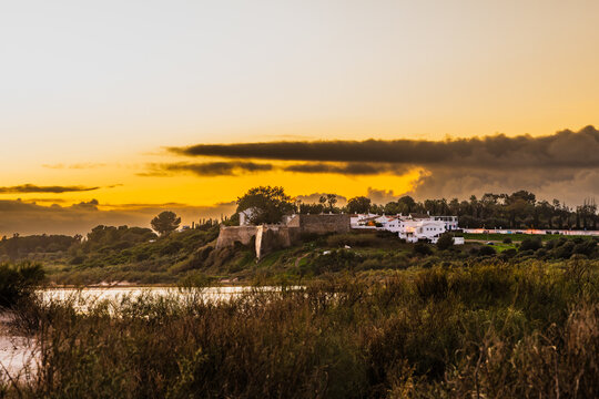 The historic village of Cacela Velha glows under a golden sunset sky, with its ancient fort and whitewashed houses. - Powered by Adobe