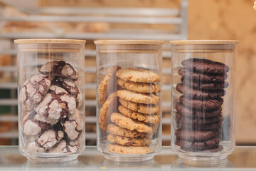 Three glass jars filled with different types of chocolate and oatmeal cookies on a bakery shelf,...