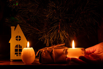 New Year's tree and gift wrapped in kraft paper with the Ukrainian flag and a woman's hand holding a candle at home