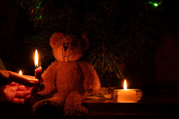 New Year tree and a woman's hand holding a candle near the tree and a child's teddy bear in the dark