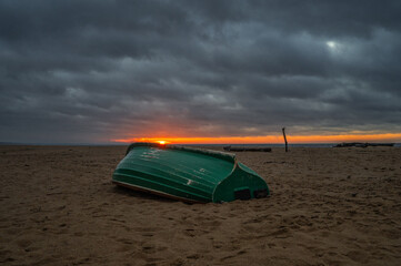Green overturned boat on sandy beach at dramatic Baltic Sea sunset
