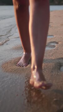 Woman barefoot legs close up walking sand beach along sea shore. Water waves splashing, sunset soft light. Outdoor lifestyle travel on summer holiday vacation. Concept relax freedom. POV slow motion