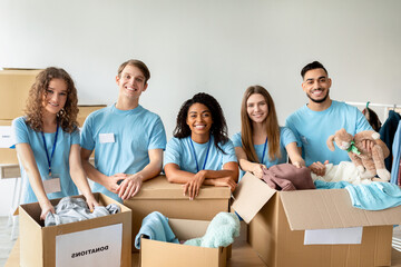 Young volunteers work together in a charity center, sorting clothing donations. They are smiling and engaged, demonstrating teamwork and joy in helping others. This moment captures community spirit.