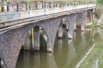 Fototapeta premium an arched bridge spanning over an artificial lake. The bridge features several stone arches and concrete pillars that extend into the water.