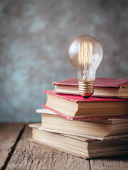 Glowing Vintage Edison Light Bulb Balanced on Stack of Antique Hardcover Books for Concept of Creative Inspiration New Ideas Literary Wisdom Academic Research Education and Knowledge Heritage Themes
