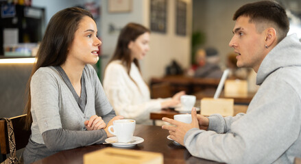Couple of young guy and woman chatting and drinking coffee at table in cafe