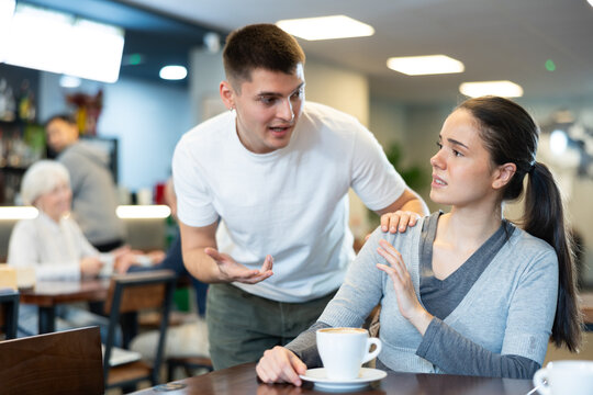Young woman is sitting at a cafe table, drinking delicious coffee and refusing to meet the guy who approached her, she ignores him