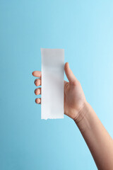 Hand holding blank paper receipt on blue background with copy space, minimalist mockup for billing, expense documents, refunds, and financial design