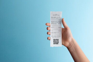 Hand holding paper receipt with qr code on blue background, representing digital payments, expense documentation, receipt scanning, and paperless accounting workflow