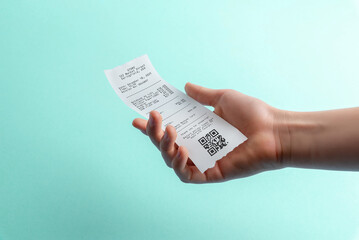 Hand holding paper receipt with qr code on blue background, digital payment and expense tracking concept for fintech apps, accounting software, and receipt management