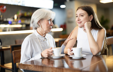 Elderly woman comforts young woman and drinking coffee at table in cafe