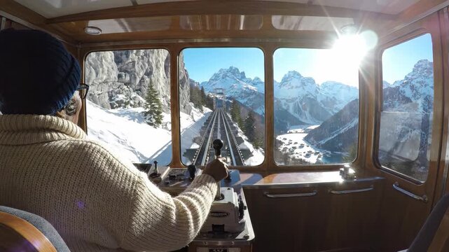 Woman operating a funicular through snowy mountains with increasing sunflare for travel and alpine adventure