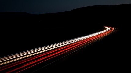 Nighttime long exposure shot of vehicle taillights on a winding highway, contrasting the dark landscape