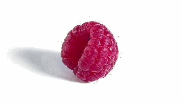 A close-up shot of a single, plump, bright red raspberry with a textured surface, slowly spinning on a clean white background