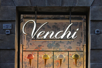Naklejka premium SIENA, ITALY – OCTOBER 7, 2025: Venchi shop window with ice cones in different colours in antique building. Venchi is an Italian chocolate and gelato brand since 1878