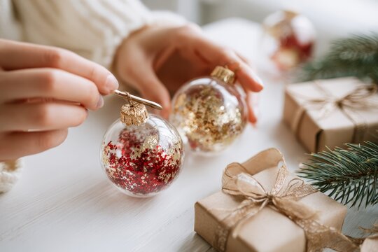 Woman painting white snowflake design on Christmas bauble for cozy holiday home decor.