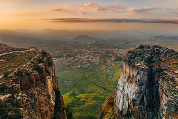 Aerial view of a dramatic escarpment and valley at sunset, with steep cliffs, vast plains, and distant mountains, overlooking the Tundavala Gap from Serra da Leba in Huíla Province, Angola. 
