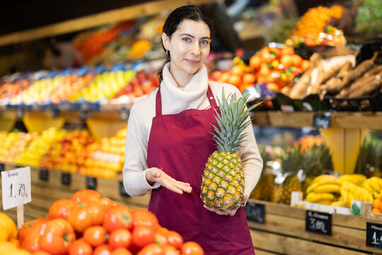 Saleswoman offers a ripe pineapple in a supermarket. Supermarket employee checks the quality of the pineapples and puts them on the counter