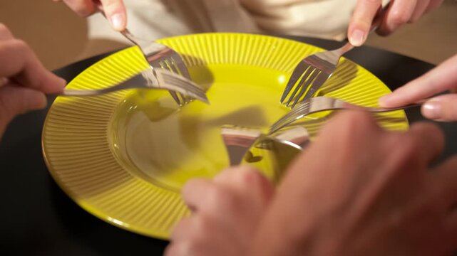 People fighting with forks for a single pea on a plate. Several hands with forks fiercely fighting over a single pea on a yellow plate, symbolizing scarcity, competition for resources, food insecurity