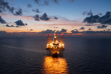 Aerial view from a drone of big jack up offshore drilling oil rig, production platform and supply vessel In the ocean during sunset - Oil and Gas Industry