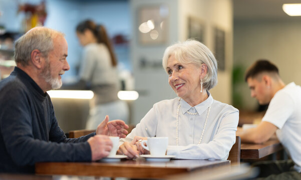 Senior woman in cafe sits opposite male colleague in cafe, chat and joke, drinking wine, spend time. Date, romantic meeting, nice time together. Atmosphere of cafe, restaurant conducive communication