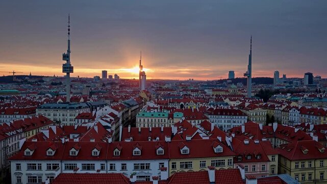 A vibrant city skyline features distinct towers reaching for the cloudy twilight sky as colors shift in the background. Rows of charming buildings, with red rooftops, create a pict