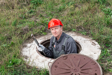 A plumber peers out from an open water well in a rural area. Plumbing repair and maintenance