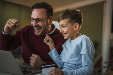 Happy father and son celebrating online shopping success at home