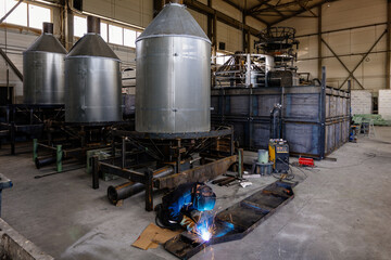 Industrial worker in protective mask welding steel parts of heating oven