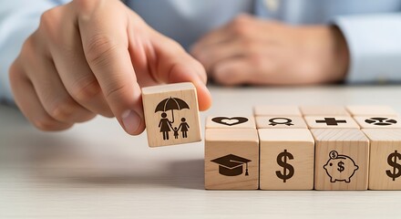 Hand placing a wooden block with family and umbrella icon among other financial and life planning symbols.