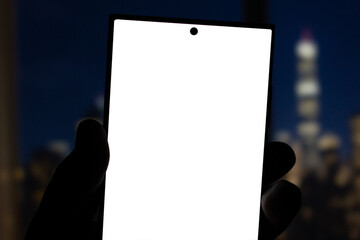 Hand holding smartphone with blank screen with city at night behind