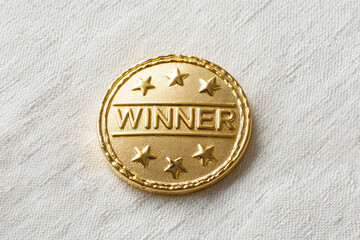 Shiny gold winner pin badge represents joyful victory success achievement. Round metal object symbolizes pride competition reward. Triumphant first place champion celebration on white texture