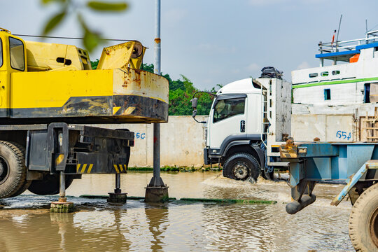 A trailer truck carrying a load covered with a tarpaulin is parked at the port with its reflection in the tidal flood waters.