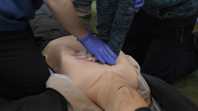 hands performing chest compressions on mannequin during emergency training session, blue gloves and instructor guiding technique in indoor simulation, focus on torso depth and rhythm