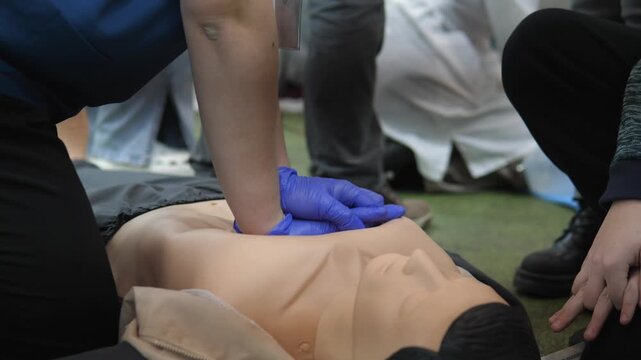 trainee performing continuous chest compressions on mannequin in handson CPR drill, blue gloves, focus on depth and cadence, group training atmosphere with instructor supervision