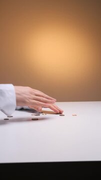 Vertical video doctor in a medical gown holding an empty wallet, with a few coins falling onto a white surface, representing financial struggles and healthcare costs