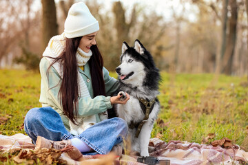 Beautiful young woman with cute husky dog having picnic in autumn park